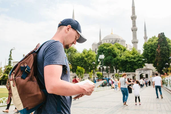 Ein Reisender mit Baseballmütze und Rucksack blickt auf die Landkarte neben der blauen Moschee - dem berühmten Anblick von Istanbul. Reisen, Tourismus, Sightseeing. — Stockfoto