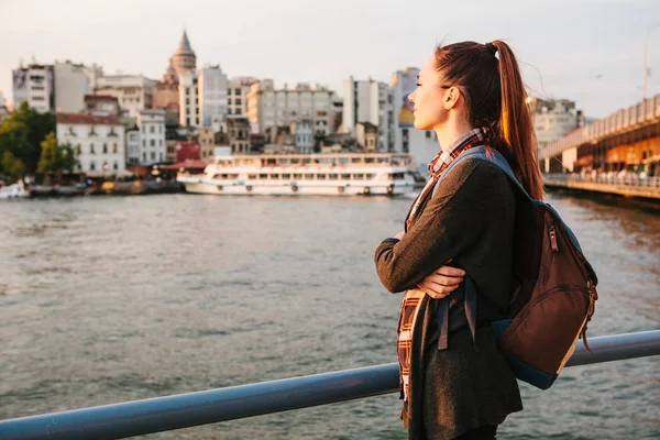 Young beautiful tourist girl with a backpack at sunset next to the Bosphorus on the background of Istanbul. Turkey. Rest, vacation, hiking. — Stock Photo, Image