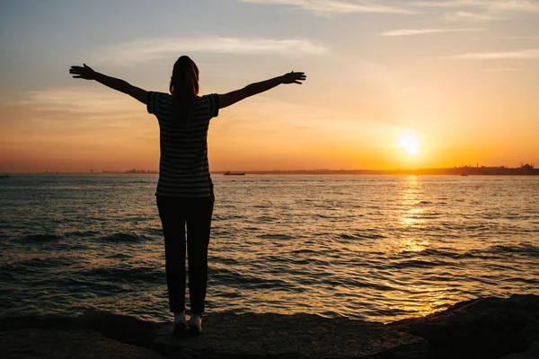 Genç kız arka yanında deniz günbatımı arka plan karşı ellerini kaldırdı. Özgürlük, dinlenme, seyahat, tatil. Siluet