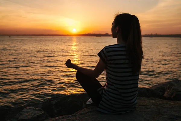 Genç güzel kız pratik Yoga ve gün batımında denize yanında buzlu meditasyon. Spor. Yoga. Meditasyon. Rekreasyon. Tatil. Gevşeme.