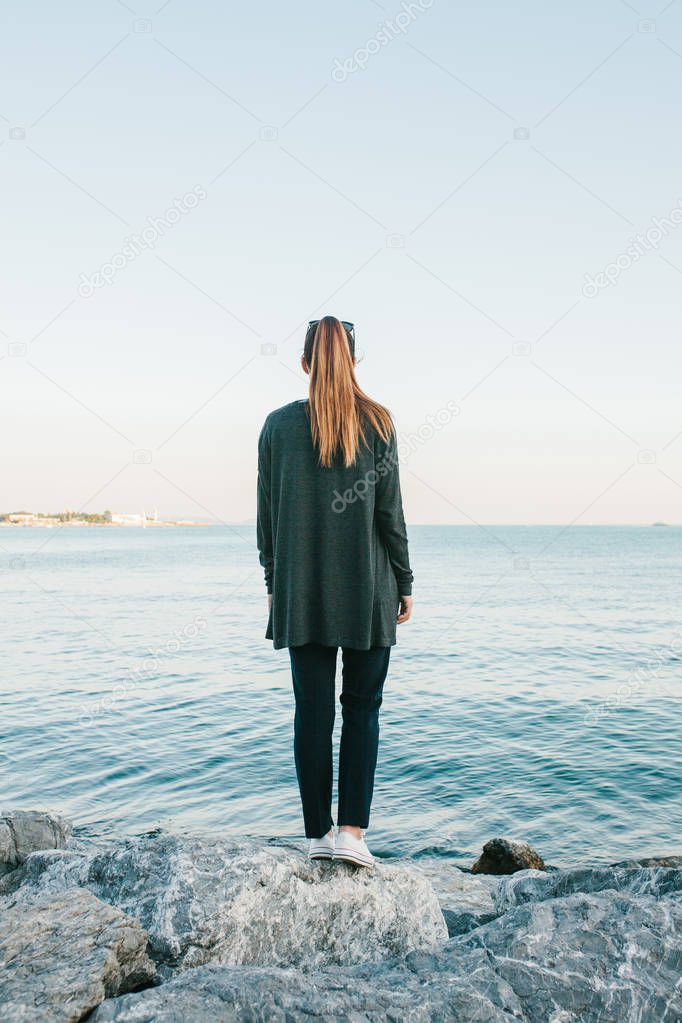 The girl stands on the rocks on the coast of the Bosphorus and looks into the distance and dreams. View from the back. Rest, solitude.