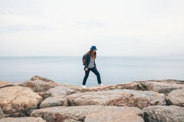Bir gezgin bir sırt çantası ile şapkalı bir denizin yanında yürüyor. Seyahat, turizm, özgürlük.