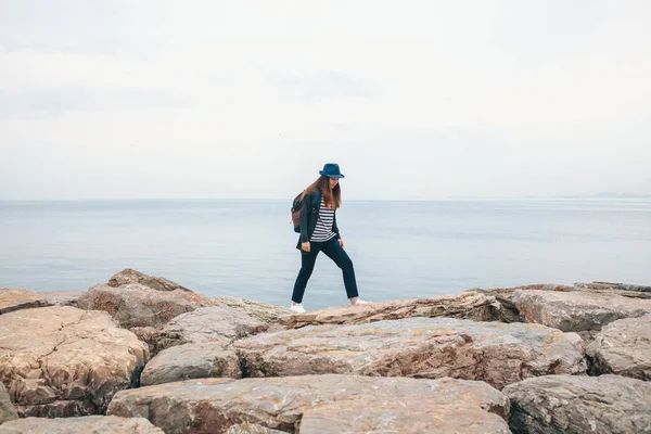 Bir gezgin bir sırt çantası ile şapkalı bir denizin yanında yürüyor. Seyahat, turizm, özgürlük.