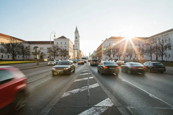 Kilátás az út az utcai Leopoldstrasse München - a Németország Bajorország fővárosa. Homályos gyors autó naplemente háttér. — Stock Fotó