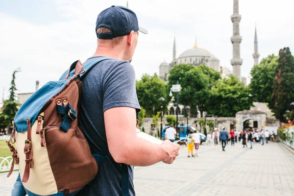 Путешественник в бейсболке с рюкзаком смотрит на карту рядом с синей мечетью - знаменитой достопримечательностью Стамбула. Путешествия, туризм, осмотр достопримечательностей . — стоковое фото