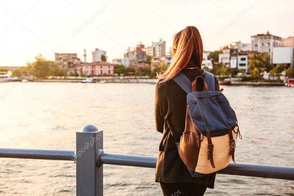 Young beautiful tourist girl with a backpack at sunset next to the Bosphorus on the background of Istanbul. Turkey. Rest, vacation, hiking.