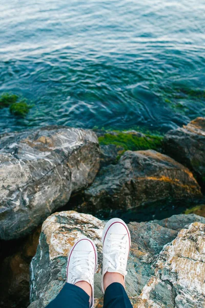 Füße in weißen Turnschuhen auf dem Felsen stehend, schöne Aussicht auf welliges Wasser — Stockfoto
