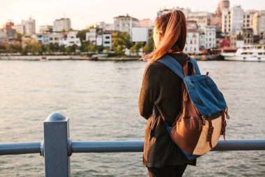 Istanbul 'un arka planda bir sırt çantası-günbatımında Boğaz'ın yanındaki genç güzel turist kızla. Türkiye. Dinlenme, tatil, hiking.