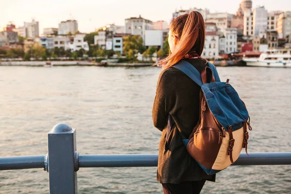 Young beautiful tourist girl with a backpack at sunset next to the Bosphorus on the background of Istanbul. Turkey. Rest, vacation, hiking. — Stock Photo, Image
