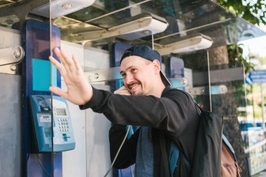 Genç, çekici, modern bir adam bir Ankesörlü telefon konuşuyor ve eliyle ağırlıyor. İletişim kavramı.