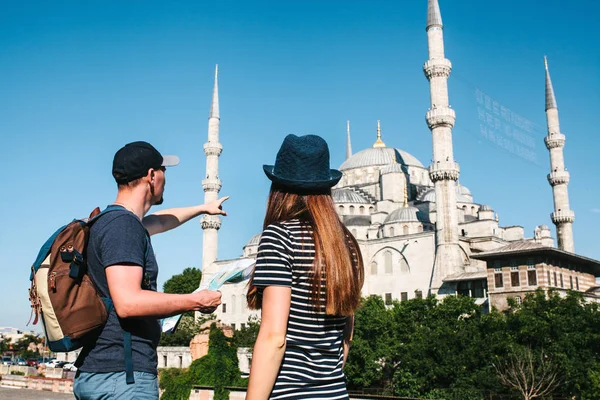 Pár turistů, mladý muž a hezká žena podívat na mapu vedle světově proslulé modré mešity zkratka Sultanahmet v Istanbulu v Turecku. Muž ukazuje jeho ruku směrem. — Stock fotografie