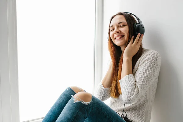 Piękna dziewczyna jest słuchanie muzyki obok okna — Zdjęcie stockowe