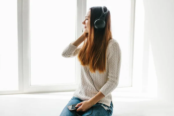 Menina bonita está ouvindo a música ao lado da janela — Fotografia de Stock