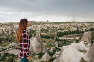 Genç bir kadın üzerinde yüksek bir noktada duruyor ve Kapadokya'nın tepelerde Yağmurlu hava görünümünü bakar. Harika bir manzara.