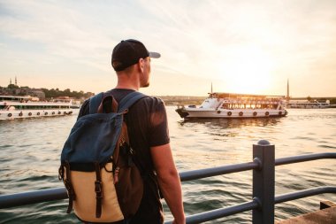 Erkek turist Istanbul'da Boğaz'ın yanındaki günbatımında bir sırt çantası ile. Hiking, tatil eğlence kavramı.