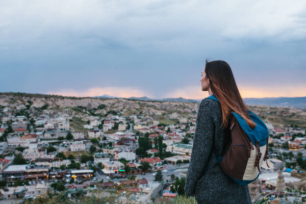 Young woman tourist from a high point looking at the sunset over the town and dreaming. Tourism, rest, vacation.
