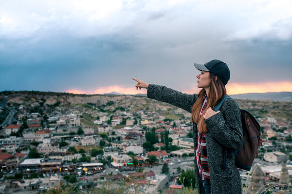 Young woman tourist with high point showing hand at sunset over the city of Goreme in Turkey. Cappadocia. Tourism, rest, vacation.