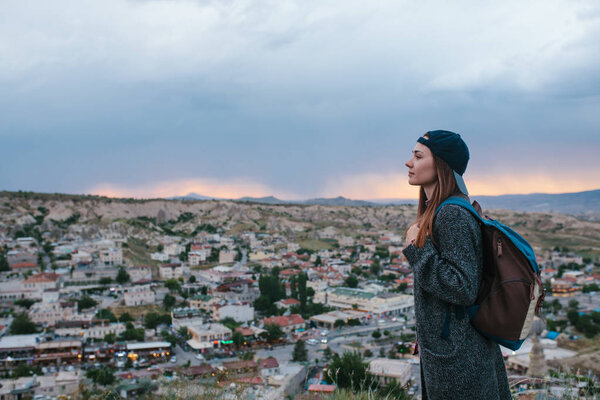 Young woman tourist stands on a sunset background over the city of Goreme in Turkey. Cappadocia. Tourism, rest, vacation.