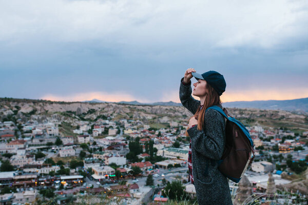 Young woman tourist stands on a sunset background over the city of Goreme in Turkey. Cappadocia. Tourism, rest, vacation.