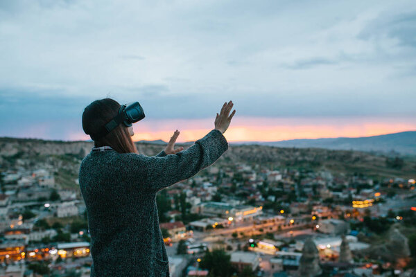A woman in virtual reality glasses on the background of a sunset over the city. Concept of future technologies. Modern technologies.