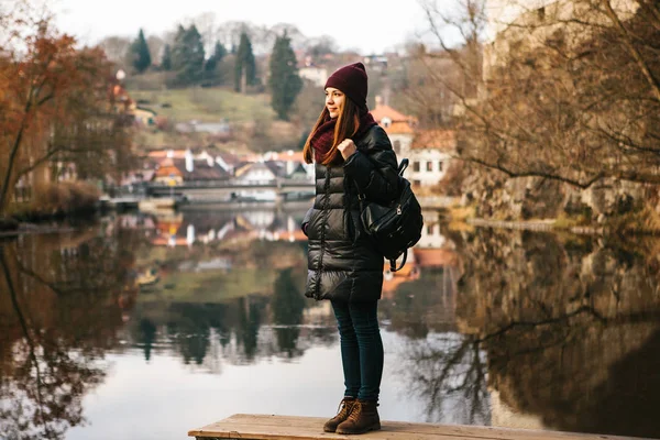 A tourist girl with a backpack standing on the shore and enjoying the nature and views of the city of Cesky Krumlov in the Czech Republic. The concept of solo travel. — Stock Photo, Image