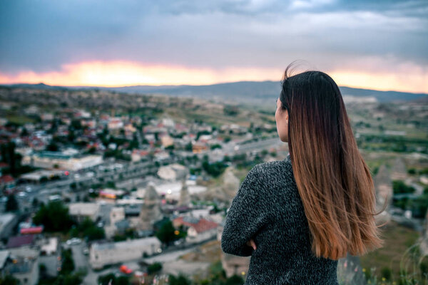 Young woman tourist from a high point looking at the sunset over the city of Goreme in Cappadocia in Turkey and dreaming. Tourism, vacations, rest.