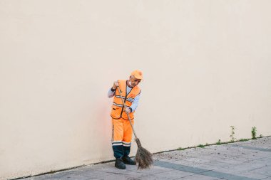 Istanbul, June 15, 2017: Janitor in bright orange uniform sweeping the tile on the street in Sultanahmet district clipart