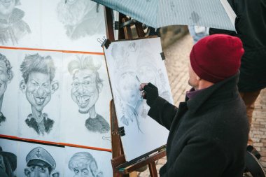 Prag, 24 Aralık 2016: Street Sanatçı karikatürist Prag'da turistler için kırmızı bere berabere Portreler