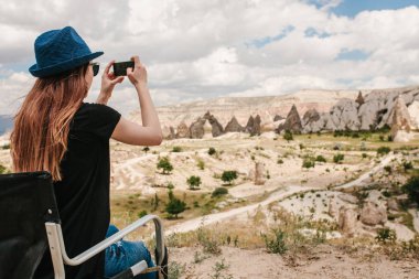 Bir turist kız telefonda hills Kapadokya Türkiye'de güzel bir manzarasına anısına bir fotoğraf yapar. Seyahat, turizm, hiking tatil.