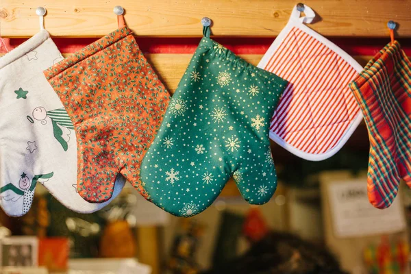 Christmas mittens potholders hang in kitchen against the background of blurry kitchen appliances. — Stock Photo, Image