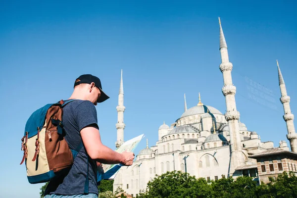 Cestovatel v baseballovou čepici s batohem se dívá na mapě vedle modré mešity - slavný pohled z Istanbulu. Cestování, Turistika, Památky. — Stock fotografie