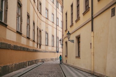 Turist kız güzel ıssız dar cadde boyunca Prag'da iki tarihi binalar arasında yeşil ceket giriyor