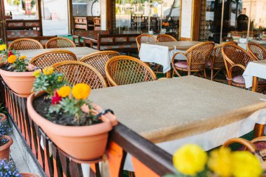 Hasır sandalyeleri ve ahşap mobilyalarla tencere bitkiler ve çiçekler ile yanındaki boş açık yaz kafe görünümünü.