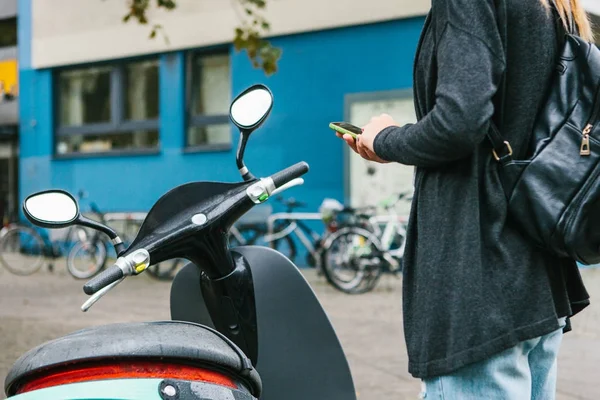 A tourist with a backpack is going to use an electric scooter through a mobile application in the phone and distally activate it. A popular vehicle in Berlin and Paris. — Stock Photo, Image