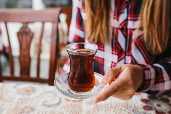 Hermosa joven sentada en la mesa en un café al aire libre y beber té de vaso de precipitados —  Fotos de Stock