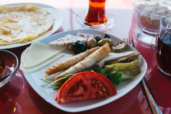 Plate with vegetarian food - bread roll with fresh vegetables cheese and olives next to glass with drink on red cafe table