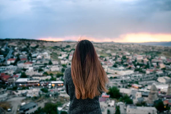 Jonge vrouw toeristische van een hoog punt kijken naar de zonsondergang over de stad van Goreme in Cappadocië in Turkije en dromen. Toerisme, vakanties, rust. — Stockfoto