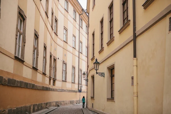 Chica turística en chaqueta verde camina a lo largo de hermosa calle desierta estrecha en Praga entre dos edificios históricos — Foto de Stock