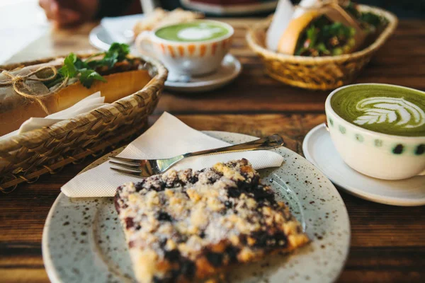 Здоровый завтрак в ресторане: чашки зеленого чая с молоком, десерт и сэндвичи с овощами и травами на деревянном столе . — стоковое фото