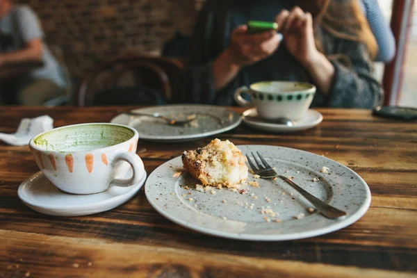 A dirty plate and an empty cup of coffee. The half-eaten cupcake on a plate. Empty dishes after eating on a wooden table. On the background of a girl in a cafe — Stock Photo, Image