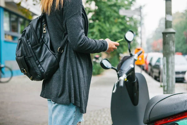 Un turista con uno zaino utilizzerà uno scooter elettrico attraverso un'applicazione mobile nel telefono e lo attiverà distalmente. Un veicolo popolare a Berlino e Parigi . — Foto Stock