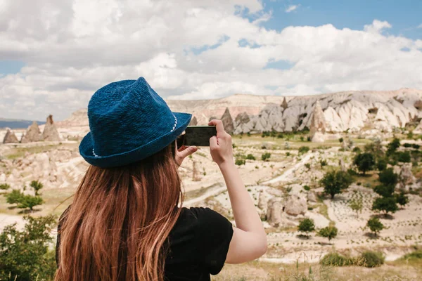 Una chica turista hace una foto en el teléfono en memoria de una hermosa vista de las colinas de Capadocia en Turquía. Viajes, turismo, senderismo, vacaciones . — Foto de Stock