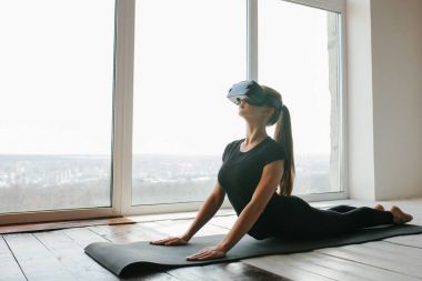 Sanal gerçeklik gözlüklü genç güzel kız yoga ve aerobik uzaktan yapar. Geleceğin teknolojisi kavramı. Modern görüntüleme teknolojisi. Sınıflarda spor uzaktan tek.