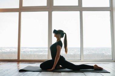 Sanal gerçeklik gözlüklü genç güzel kız yoga ve aerobik uzaktan yapar. Geleceğin teknolojisi kavramı. Modern görüntüleme teknolojisi. Sınıflarda spor uzaktan tek.