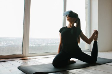 Sanal gerçeklik gözlüklü genç güzel kız yoga ve aerobik uzaktan yapar. Geleceğin teknolojisi kavramı. Modern görüntüleme teknolojisi. Sınıflarda spor uzaktan tek.
