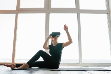 Sanal gerçeklik gözlüklü genç güzel kız yoga ve aerobik uzaktan yapar. Geleceğin teknolojisi kavramı. Modern görüntüleme teknolojisi. Sınıflarda spor uzaktan tek.