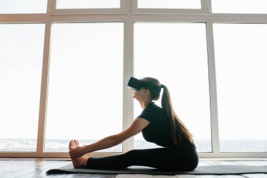 Sanal gerçeklik gözlüklü genç güzel kız yoga ve aerobik uzaktan yapar. Geleceğin teknolojisi kavramı. Modern görüntüleme teknolojisi. Sınıflarda spor uzaktan tek.