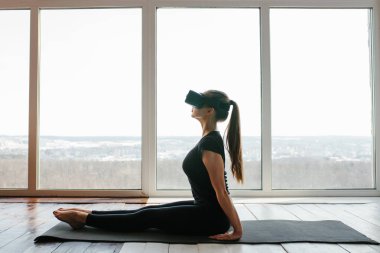 Sanal gerçeklik gözlüklü genç güzel kız yoga ve aerobik uzaktan yapar. Geleceğin teknolojisi kavramı. Modern görüntüleme teknolojisi. Sınıflarda spor uzaktan tek.
