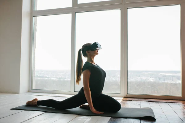 Een mooi meisje in virtual reality-bril maakt yoga en aerobics op afstand. Technologie van de toekomst concept. Moderne imaging technologie. Klassen in één sport op afstand. — Stockfoto