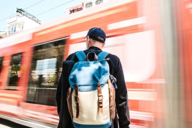 Yol tramvay ile önünde dostum. Sırt çantası ile rahat kıyafetler erkek turist önünde duruyor yol tramvay ile güneşli yaz günü geçiyor. Hareket Bulanıklığı.